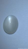 Pearl white oval catseye moonstone cabochon showing distinctive catseye reflection due to chatoyancy effect.