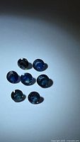 Seven round cut natural blue sapphires arranged in a cluster on a plain surface showing their blue color and facets.