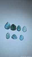 Seven natural blue, leaf-cut tourmaline gemstones arranged in two rows showing various cut leaf shapes and blue tones.