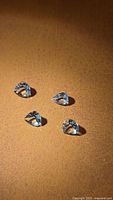 Four pear-shaped natural Brazilian aquamarine gemstones placed on a brown textured surface, showing their teardrop cut and light blue clarity.