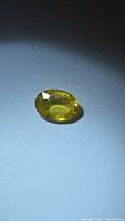 Oval cut natural yellow sapphire gemstone, 0.90 carat, placed on white surface.