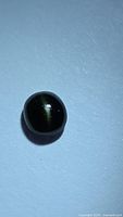 Image showing oval cabochon natural catseye augite gemstone with forest green color and visible catseye effect on blue background.