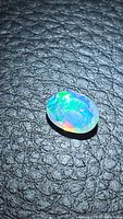 Close-up photo of a faceted oval-shaped Ethiopian opal gemstone showing multicolored flashes on a black textured background.
