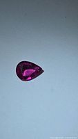 Close-up front view of the teardrop-shaped hot pink tourmaline gemstone on white background.