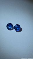 Top-down photo of two round faceted cornflower blue kyanite stones showing color and clarity.