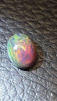 Oval black opal cabochon showing red and green play-of-color