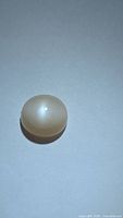 Photo of a smooth oval cabochon peach moonstone showing catseye effect on a plain background.