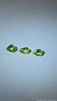 Three natural apple green peridot gemstones, pear-shaped, shown under direct light to highlight color and clarity.