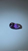 Single deep purple pear-shaped amethyst gemstone photographed on white background, showing facets and shape.