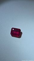 Natural red ruby gemstone in emerald cut on a white background under normal lighting showing deep red color and clarity.