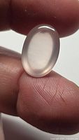 Oval cabochon rose quartz gemstone held between fingers showing size and polished surface.