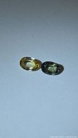Pair of natural oval cut sapphires, one green and one yellow, shown side by side on plain background.