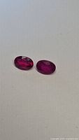 Two oval vivid red rubies against a light background showing color and cut from top and angled side views.