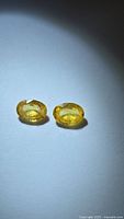 Pair of natural yellow sapphire oval cut gemstones, shown side by side on white background with close-up details of color and cut.