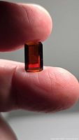 Close-up image of a deep orange octagon cut spessartite garnet held between fingers, showing its vibrant color and clarity.