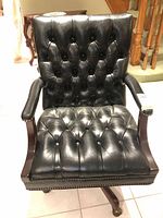 Front view showing black tufted leather, wood arms, nailhead trim