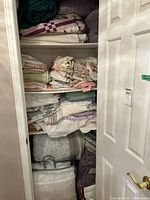 Full linen closet with multiple shelves of quilts, blankets, sheet stacks and two bagged comforters