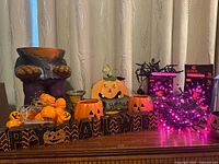 assorted Halloween décor on dresser including planter, wood sign, ceramic items, plastic pumpkin lights