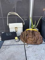 Group shot of three handbags: white patent, black satin, brown faux python