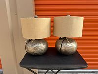 Both hammered metal lamps with shades on tabletop