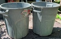 Two gray Rubbermaid Roughneck trash cans side by side showing exterior condition and rim damage