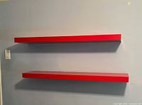 Two red floating shelves mounted on wall