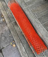 Full roll of orange plastic mesh fencing on wooden deck