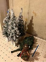 Two flocked tabletop trees, green tree sections, twig snowman on tiled floor