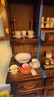 Overview of cups, saucers, bowl, wooden mills on hutch shelf