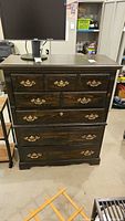 Front view of dark wood dresser showing five drawers and brass pulls