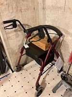 Full view of burgundy rollator walker with seat, brakes, and storage