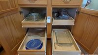 Cabinet pull-out shelves with assorted glass bakeware, mixing bowls, measuring cup, sifter, microwave lid and paper bags visible
