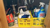Under-sink view showing two yellow crates containing Glass Plus bottle and various cleaners