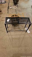 Rectangular black metal stand with plastic pot and wooden trellis visible