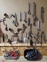 Overall pegboard view with hanging wrenches, pliers, drills and bins of tools below