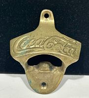 Front view of brass Coca-Cola opener showing full shape and logo