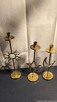 Three brass-tone metal candleholders with sun, star, moon shapes