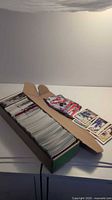 Long cardboard box filled with hundreds of hockey cards, some cards spread on lid