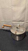 Side view of aluminum popcorn maker showing wooden handle and lid mechanism