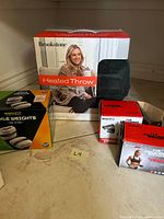 Group shot showing Brookstone heated throw box with blanket, green ankle weights box, two red ankle weight boxes