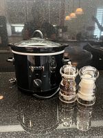 Front view of black Crock-Pot slow cooker with lid, salt and pepper grinders beside it