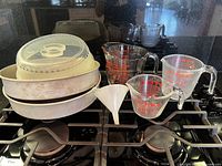 Full lot on stovetop showing baking pans, microwave cover, three Pyrex measuring cups and funnel