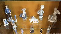 overview of 9 Lladró figurines on glass shelf