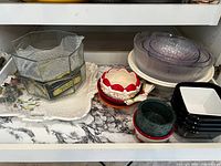Shelf view showing platter, glass vase, scalloped bowls, purple nesting bowls, black bowls and marble bowls