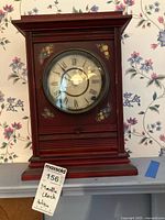 Front view of red wooden mantle clock with floral details and aged dial