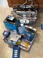 Pile showing extension cords, power strips, multimeter, boxed light bulbs
