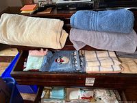 Drawer showing multiple towels: cream, rolled blue, lavender, snowman design, yellow plaid, others