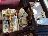 Group shot of crucifix, angel figurine, rosary beads, icon, candle, carved figure on tables