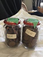 Two labeled jars filled with pennies, lids show handwritten 100