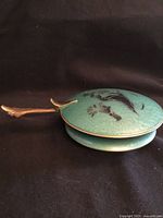 Side view of closed enameled dish showing brass-tone handle and overall condition
